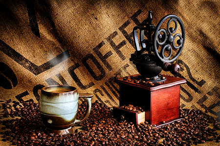 Cup of steaming hot coffee with coffee beans, coffee grinder, and coffee beans bag in background.の写真素材