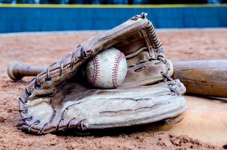 Baseball bat, glove, and ball on base on field   の写真素材
