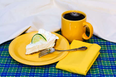 Slice of key lime pie with coffee on plate with fork and napkin.の写真素材