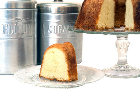 Slice of pound cake removed from whole cake which is in background along with flour and sugar canisters.  Isolated on white background with clipping path.の写真素材