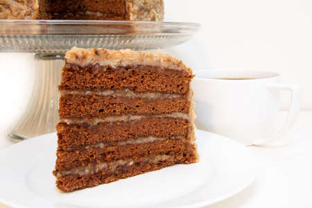 German chocolate cake slice closeup with coffee.  Slice is removed from whole cake which is in background.の写真素材