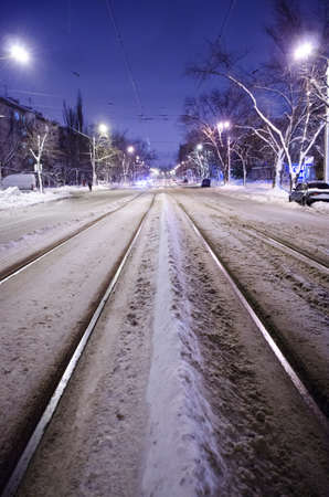 Center of the snowy road with rails. The night city with night traffic.の写真素材