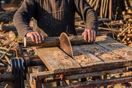 Man cutting wood using stationary circular saw outdoors in the sun.の写真素材