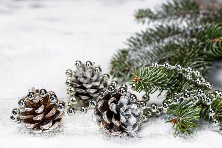 Pine cones, branch of a fir tree with and silver pearls on the wooden board covered with snow with copy space for text.の写真素材