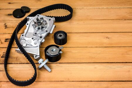 Spare parts for the car. The set of timing belt with rollers and cooling pump on a wooden background with free space for text.の写真素材