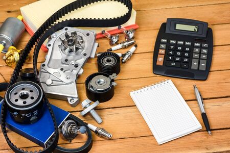 Various car parts with calculator, a block and a ballpoint pencil on the wooden table.の写真素材