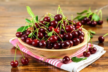 Fresh sour cherries in bowl and green leaves on wooden table.の写真素材
