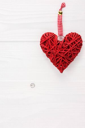 Wicker heart hanging on a white wooden board. Valentines day card concept with copy space for text.の写真素材