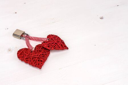 Two red hearts locked with a padlock on a white wooden background. Valentines day card concept.の写真素材