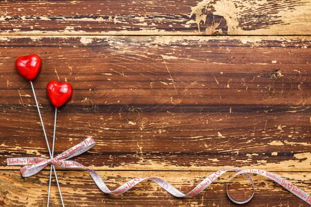 Couple of red hearts on sticks tied with a ribbon on a wooden background. Valentines day card concept.の写真素材