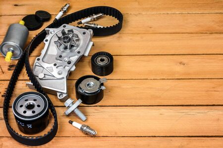 Various spare parts for the car. The set of timing belt with rollers, cooling pump, sparking plugs and filters on a wooden table with free space for text.の写真素材