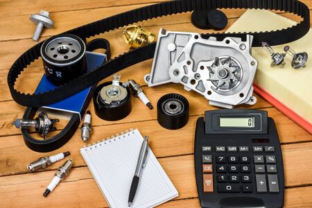 Various car parts with calculator, a block and a ballpoint pencil on the wooden table.の写真素材