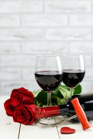 Valentine's Day concept. Red roses, wooden heart, wine bottle, corkscrew and glasses of wine on wooden blackboard.の写真素材