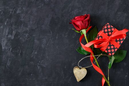 Valentines day greeting card with romantic red rose, wooden heart and gift box on dark blackboard with copy space for text.の写真素材