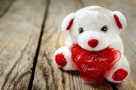 Cute white teddy bear holding a red heart and sits on an old wooden table, holiday gift for Valentine's Day.の写真素材