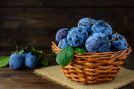 Sweet plums in a wicker basket on the wooden table with copy space for text. Selective focus.の写真素材