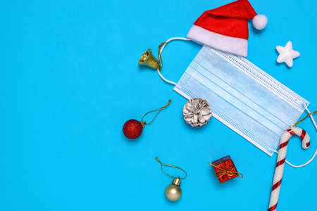 Medical mask and decorative Christmas ornaments on blue background. The concept of celebrating the...