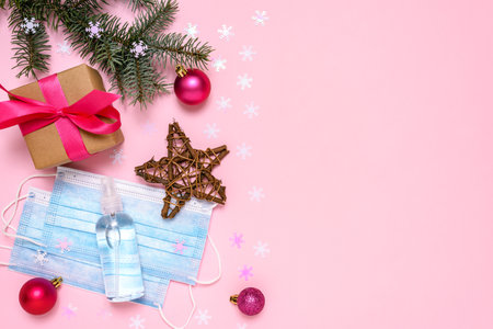 Gift box with medical face masks, antibacterial antiseptic spray for hands sanitizer and decorative Christmas ornaments on pink background. The concept of celebrating the New Year and Christmas during the COVID-19 epidemic.の写真素材