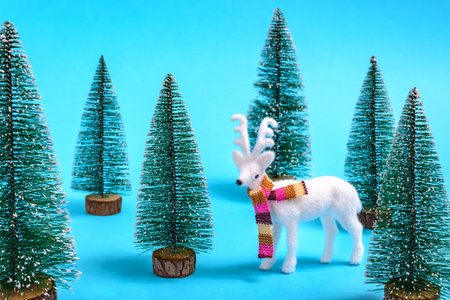 Creative winter and Christmas concept of white reindeer with a colorful scarf in a fir forest on  blueの写真素材