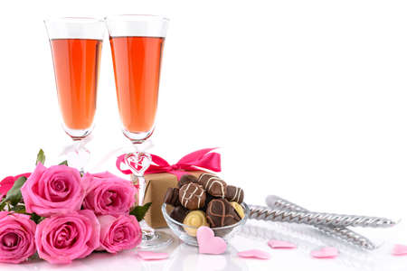 Two glasses of wine, gift box, candles, pink roses, sponge satin hearts and delicious chocolate pralines on whiteの写真素材