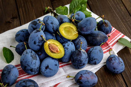 Sweet plums with green leaves on a dishcloth on the wooden table. Selective focus.の写真素材