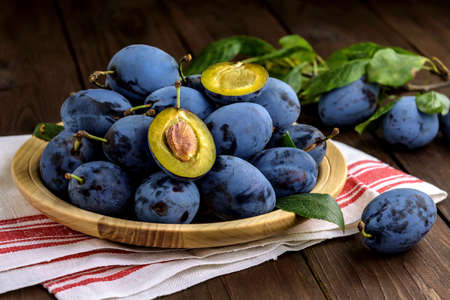 Sweet plums on a wooden plate with dishcloth on the brown table. Selective focus.の写真素材