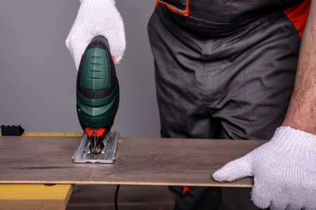Worker is cutting the laminate with an electric jigsaw. Selective focus.