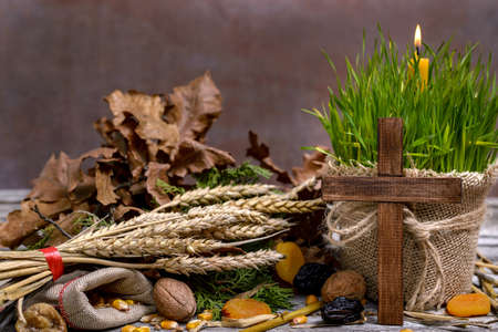 Traditional food for orthodox Christmas eve. Yule log or badnjak, cereals, dried fruit, wooden cross and a burning candle in green wheat on a wooden table. Concept celebration orthodox Christmas.の写真素材