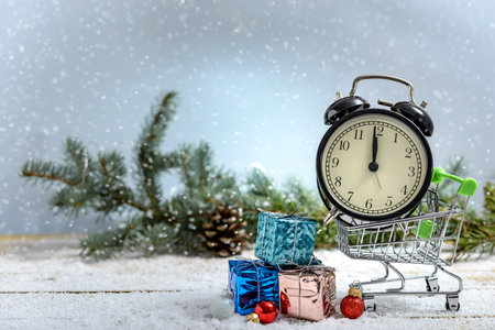 Christmas shopping concept. Alarm clock in a shopping cart and gift boxes next to fir branch while...