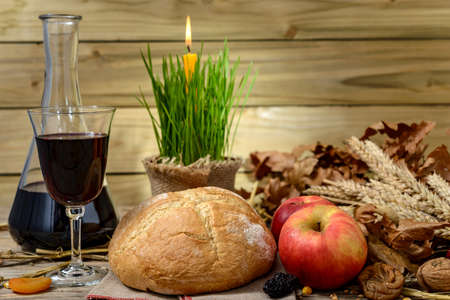 Traditional food for orthodox Christmas eve. Yule log or badnjak, apples, wine, bread, cereals, dried fruit and a burning candle in green wheat on a wooden table.の写真素材