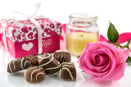 Valentine's Day concept. Delicious chocolate pralines, burning candle, pink roses and gift box on a white background. Selective focus.の写真素材