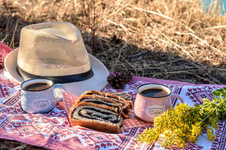 Delicious poppy seed strudel and two cups of coffee on a towel on a sunny day in nature.