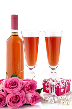 Valentine's Day concept. Bottle with two glasses of wine, pink roses, gift box and string of pearls on a white background with copy space for text. Selective focus.の写真素材