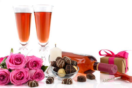 Valentine's Day concept. Two glasses of wine, gift box, pink roses, corkscrew, burning candle and delicious chocolate pralines on a white background with copy space for text. Selective focusの写真素材