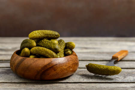 Bowl of pickled gherkins and fork with cucumber on a rustic wooden table.の写真素材