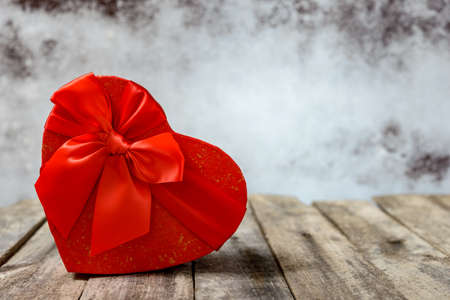 Heart shaped gift box with red ribbon on rustic wooden table for Valentine's day or celebration.の写真素材