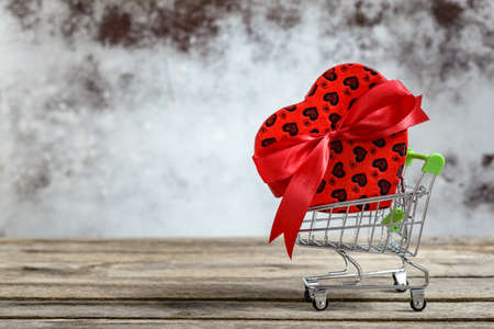 Gift box in heart shape on miniature shopping cart on wooden table. Sales and shopping concept.の写真素材