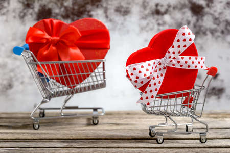 Two shopping carts with gift boxes in heart shape on a rustic wooden table. Sales and shopping concept.の写真素材