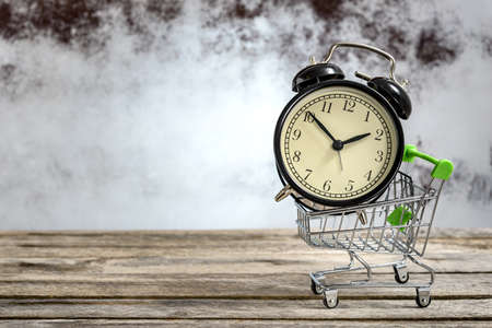 Shopping cart with vintage alarm clock on a rustic wooden table with copy space for text. Concept of sale and seasonal discounts in shopping stores.の写真素材