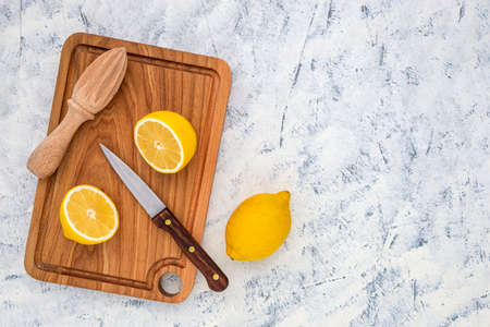 Fresh lemon cut in half with knife and juicer on wooden cutting board. Top view.の写真素材