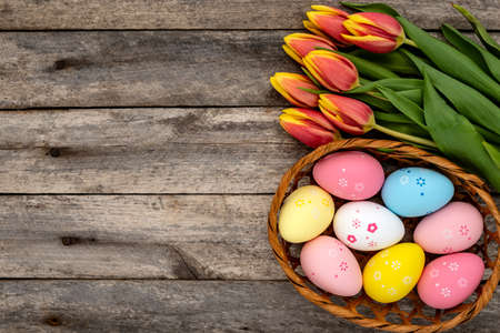 Basket of colorful Easter eggs and a bouquet of tulips on a rustic wooden table. Easter concept.の写真素材