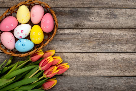 Basket of colorful Easter eggs and a bouquet of tulips on a rustic wooden table. Easter concept.の写真素材