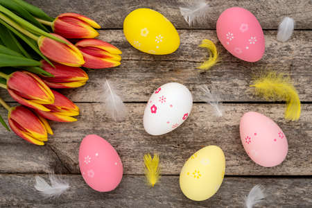 Colorful Easter eggs, feathers and a bouquet of tulips on a rustic wooden table. Easter concept.の写真素材