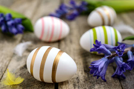 Colorful Easter eggs with feathers and blue hyacinths on a rustic wooden table. Easter concept.