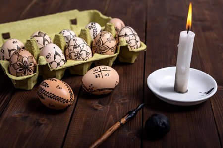 Traditionally painted Easter eggs using a fountain pen and wax in packing box ready for cooking and coloring on wooden table. Easter preparation concept.の写真素材