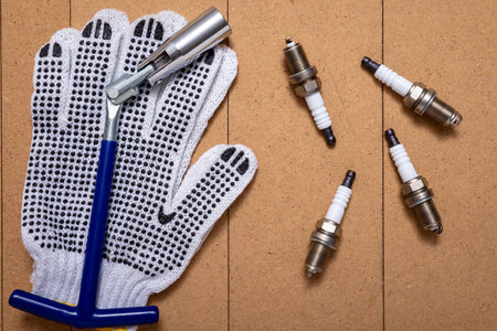 Sparking plugs, spark plug key and protective gloves on wooden table.