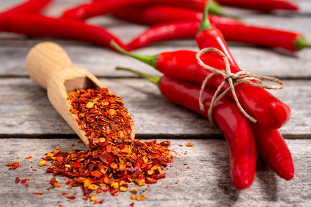 Wooden scoop with crushed chili pepper and fresh red chili pepper on old table. Selective focus.の写真素材