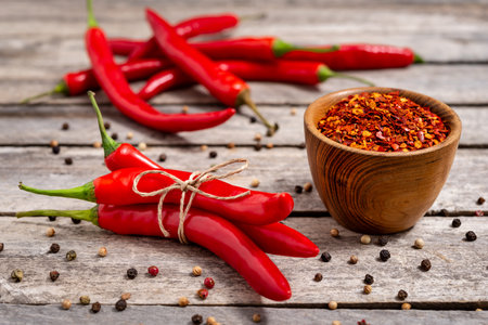 Wooden bowl with crushed chili pepper and fresh red chili pepper on old table. Selective focus.の写真素材