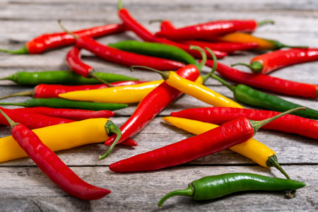 Multicolored fresh chili peppers scattered on an old table. Selective focus.の写真素材