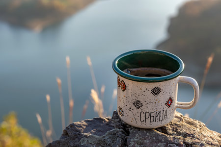 Enamel mug of coffee with the inscription Serbia on the rock on lake Rovni in Serbia. Travels concept. Selective focus.の写真素材